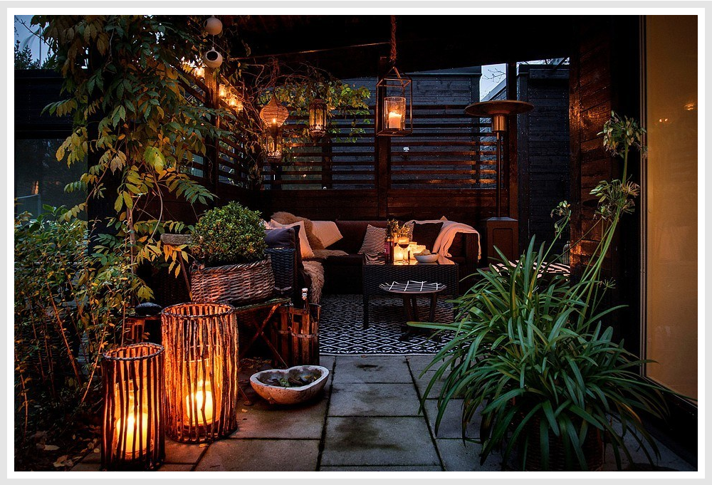 A cozily-lit patio with floor and hangin lanterns and outdoor furniture.