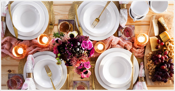 A table setting with white plates, napkins, gold-colored cutlery.