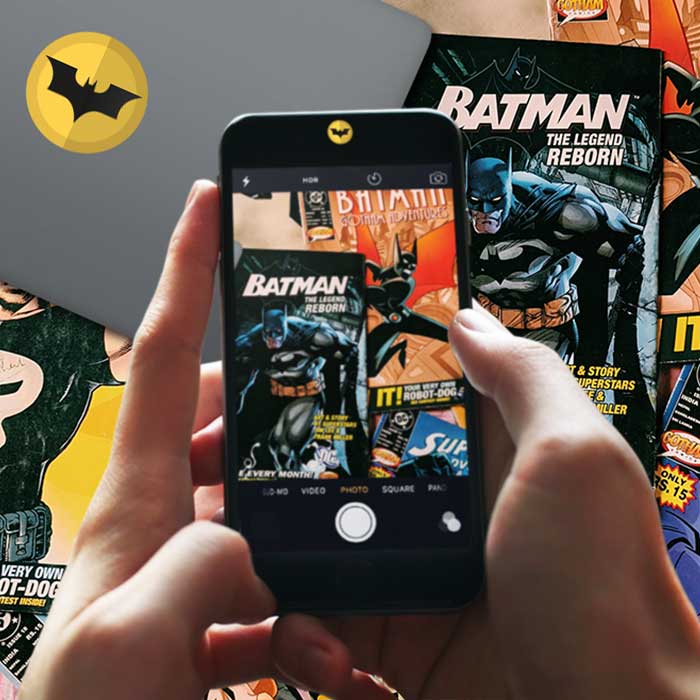 phone with superhero privacy stickers taking photo of laptop with batman sticker and comics