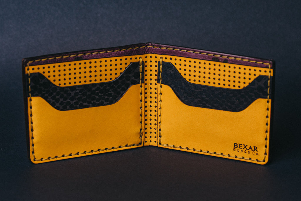 Interior of yellow and black wallet. Back yellow panel with circular perforations. Black pockets with snake print. Front yellow pockets. Wallets sitting on a black table top 