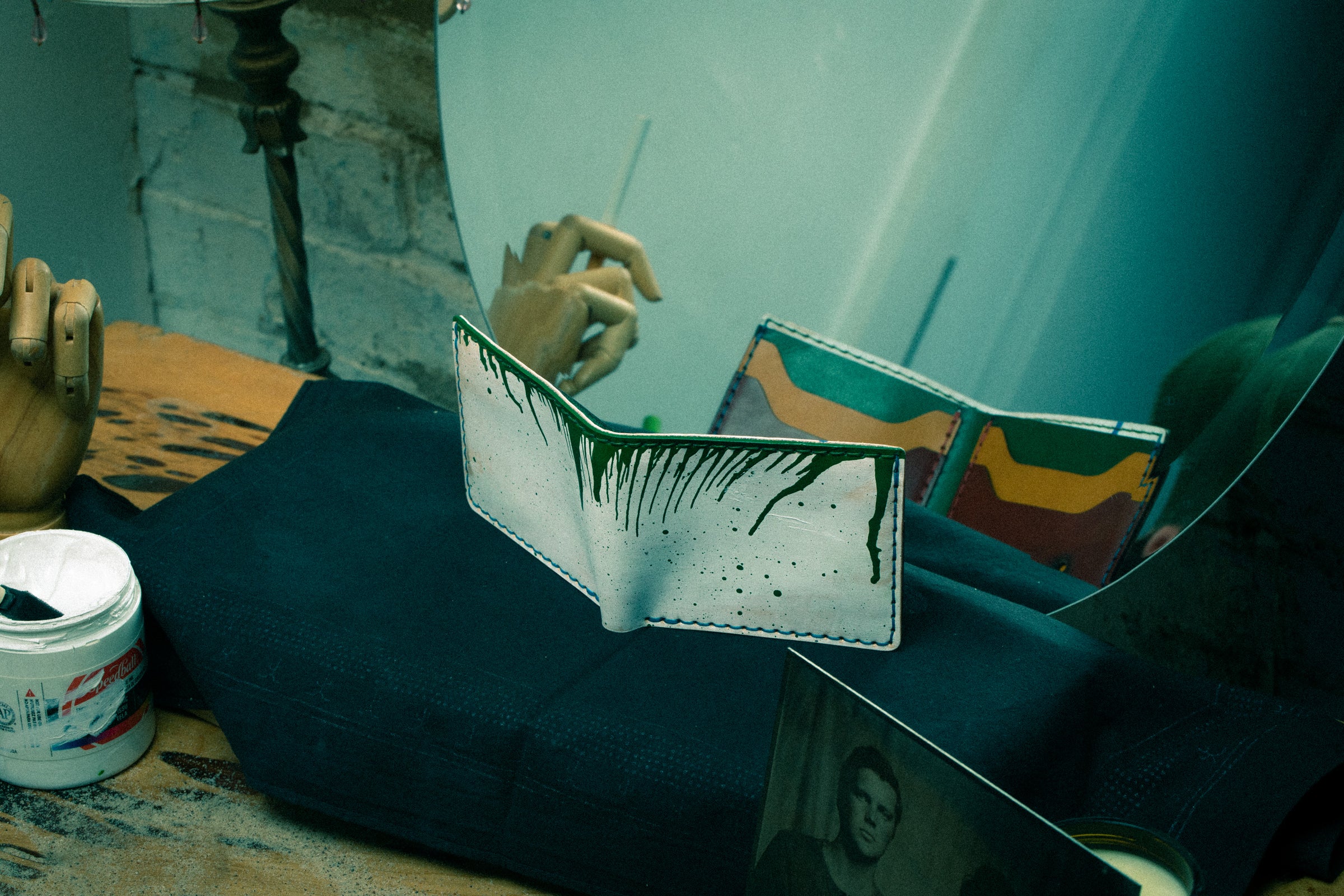 A white wallet with green paint drip sits in front of a vanity mirror.