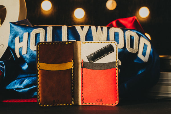 A sating jacket sits in the background as the backdrop of a custom leather wallet. This wallet has red, white, brown and yellow accents.