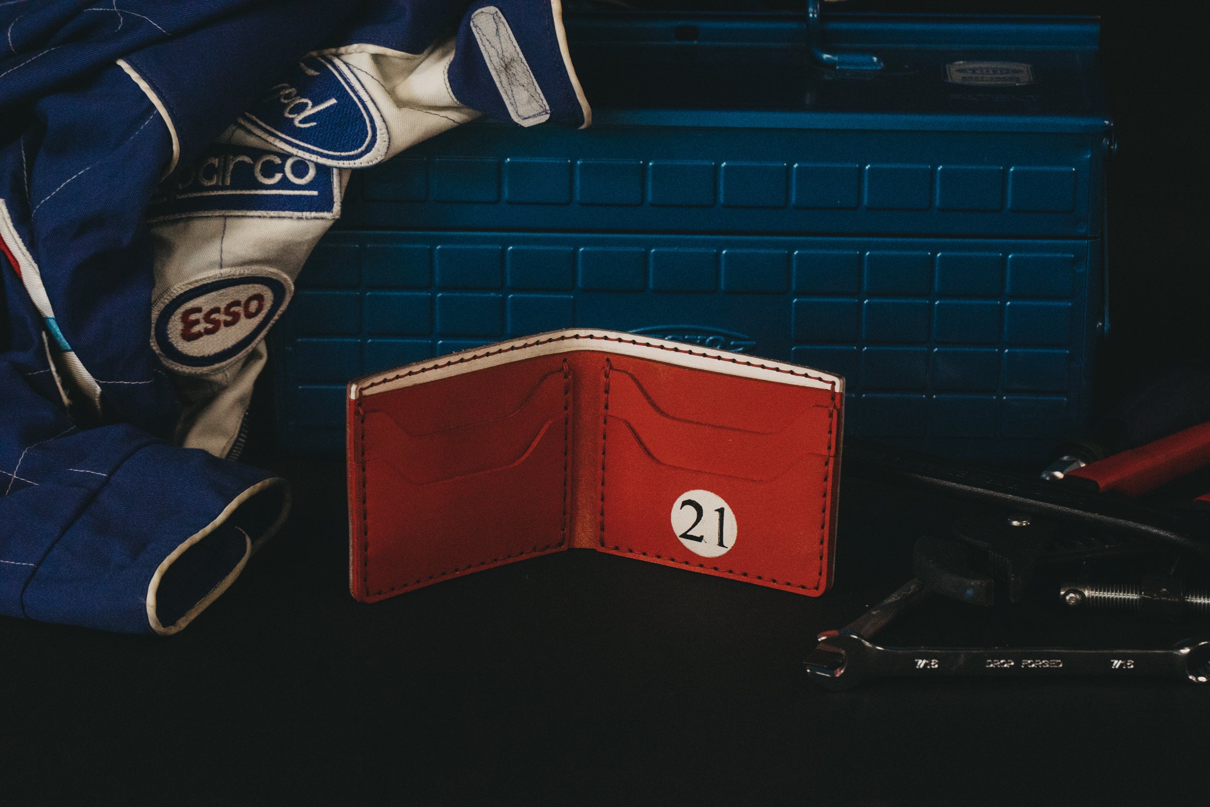 Inside of light blue mechanic theme with red interior wallet sits in front of a darker blue metal tool box with a jacket draped on top of it. 