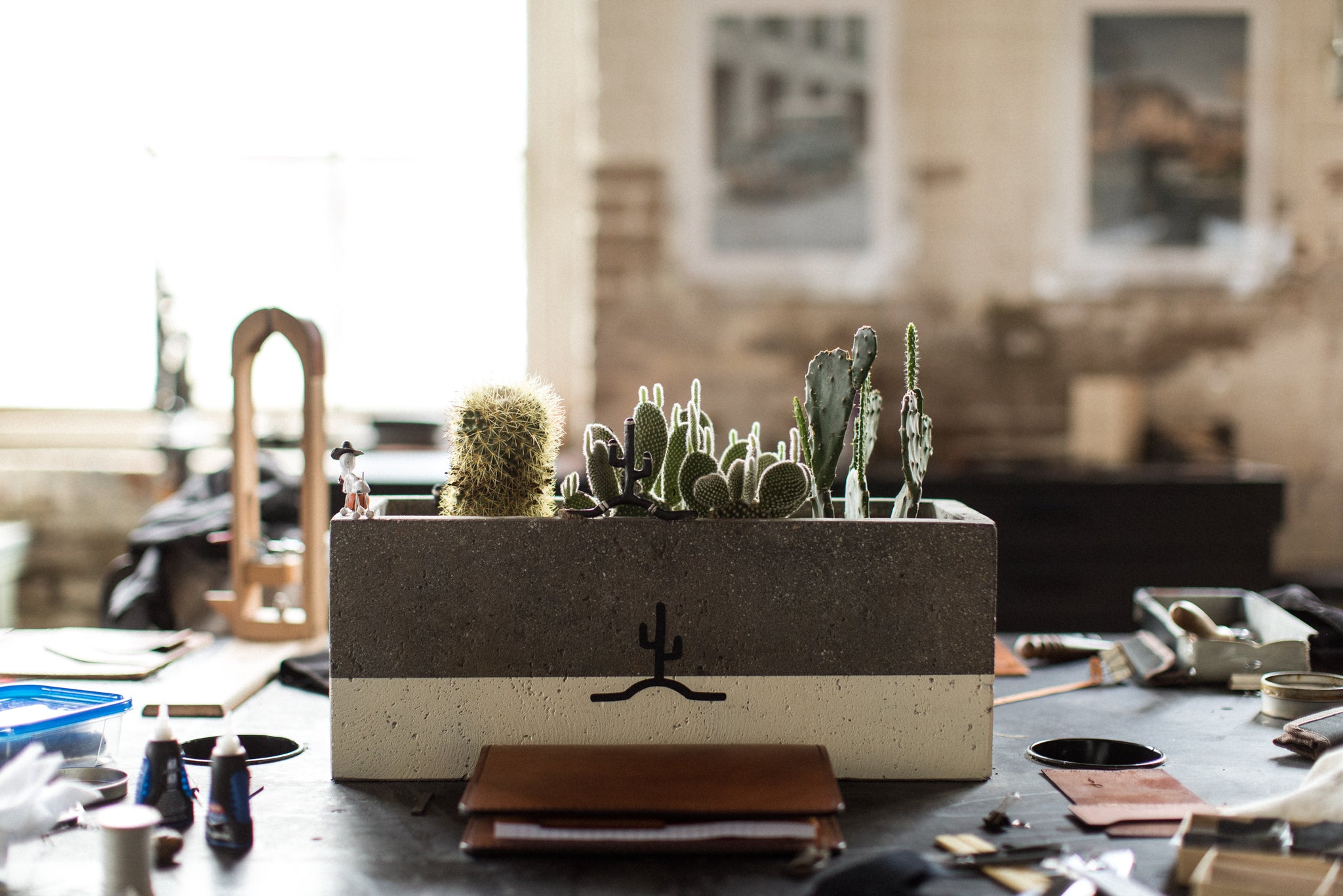 Leather items sitting on table a man working off in the distance and another man sitting behind a computer even further in the distance. A empty sofa and coffee table is visible on the left side of image.