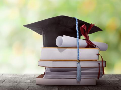 sombrero de graduación con título encima de una pila de libros