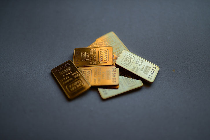 A pile of seven gold bullion bars marked ‘Credit Suisse, One Ounce Fine Gold, 999.9’ on a grey background