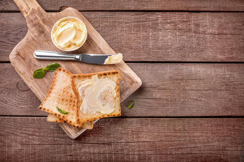 Wooden Cutting board resting on wood background. Cutting board is topped with toast, butter, and butter knife.