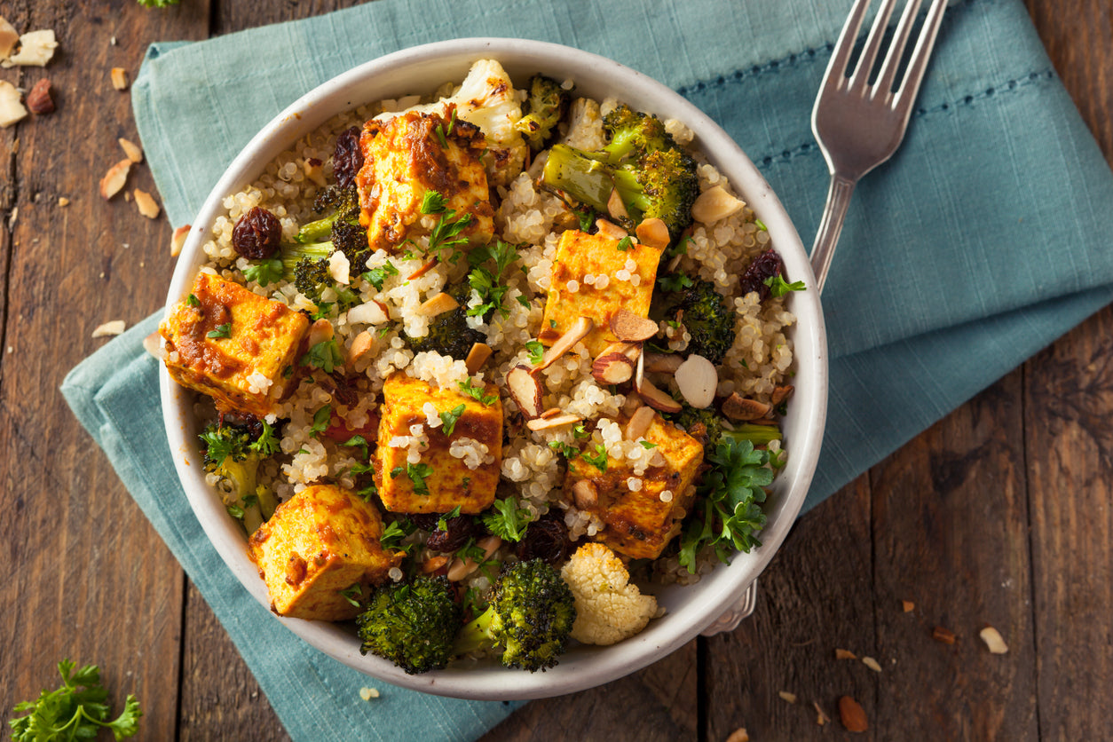 Baked tofu in a bowl with quinoa and roasted broccoli. The image is a direct overhead shot with a light blue napkin folded under the bowl and a fork resting next to it.