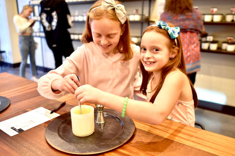 Two female children stirring a candle while visiting the store.