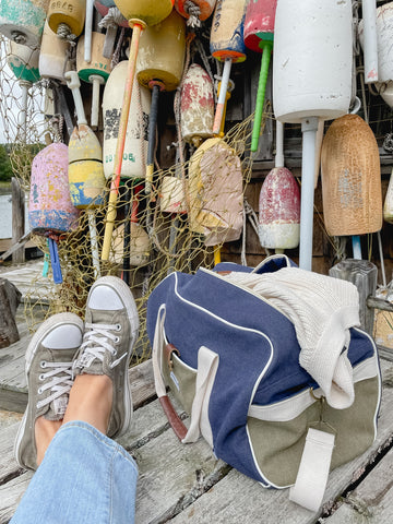 Converse shoes kicked up next to Paperboat duffel bag with colorful buoys in the background.