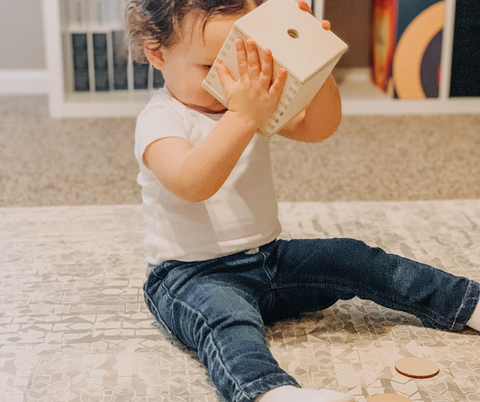 child playing with wooden toy on play mat