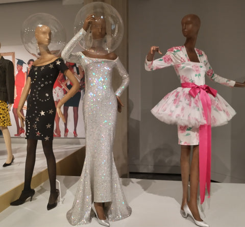 three mannequins in party dresses with two wearing large plastic space helmuts