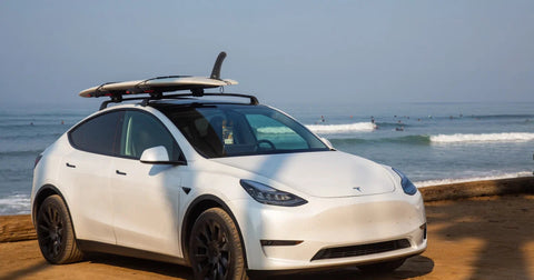 Tesla Model Y with a surfboard mounted on the roof rack