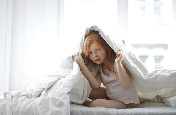 Child covering her body in a white duvet cover