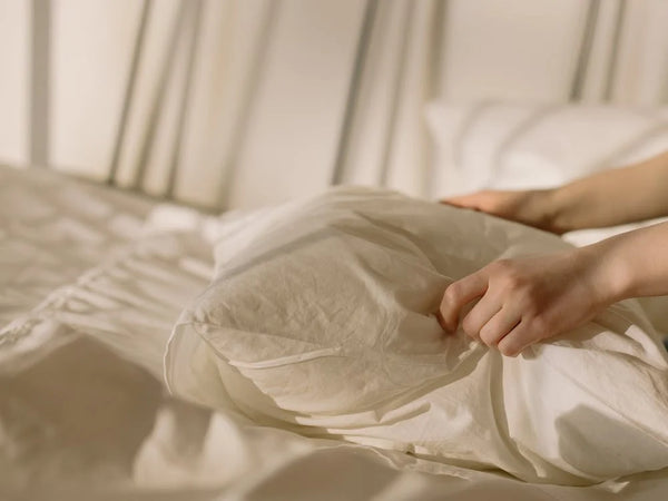 Person fixing white textile pillow on bed