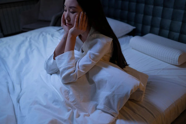 Woman in white long sleeve shirt sitting on a bed with white bed sheets