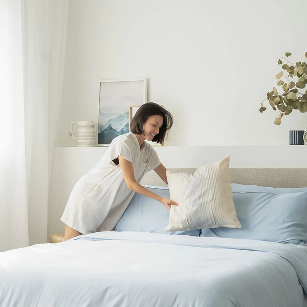 Girl fixing her bed covered in Weavve’s Signature TENCEL™ Classic Set in Sky Blue