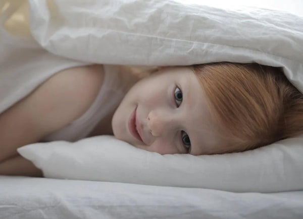 Cute girl lying on bed with her body covered in white duvet