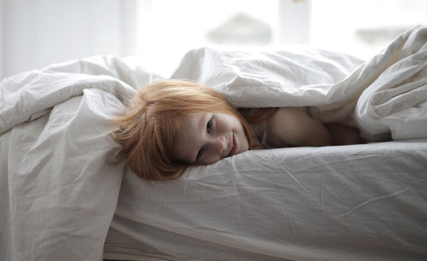 Girl lying in bed with white linen and blanket