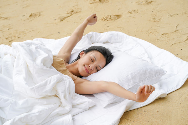 Girl stretching arms while lying on a TENCEL duvet on a beach