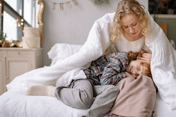 Mother and child cuddling on bed under a white duvet