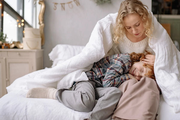 Mother and daughter cuddling on a bed under a white duvet