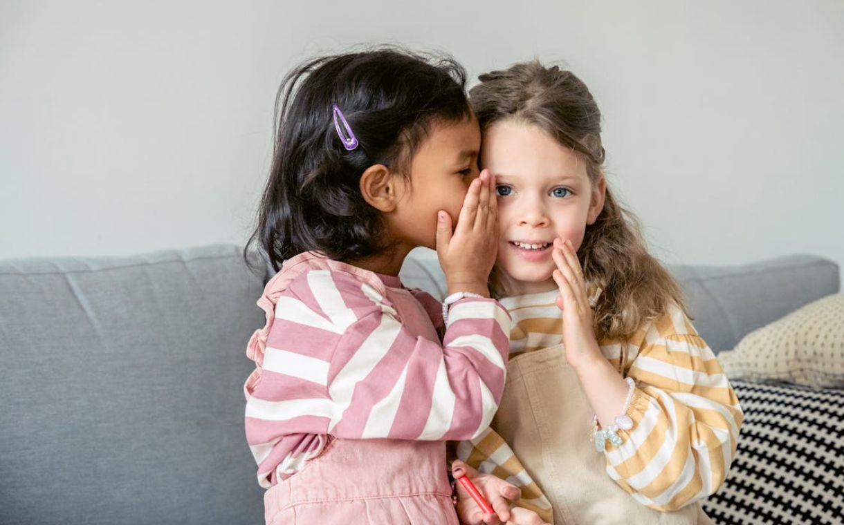 Two little girls are talking in whispers