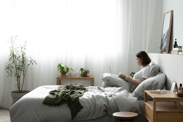 Woman reading book while sitting on ligh grey bed
