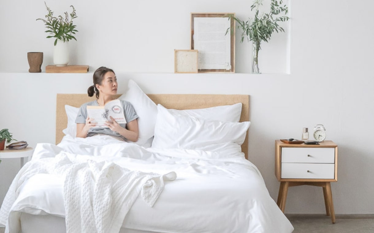 Woman sitting on bed with Weavve's white cotton bedsheets