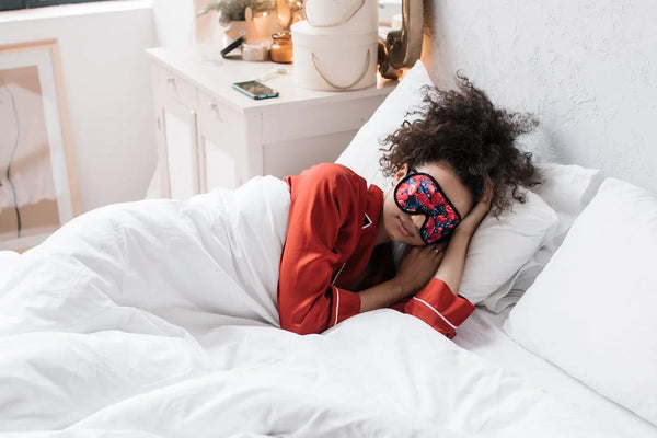 Woman wearing eye mask lying on white bed