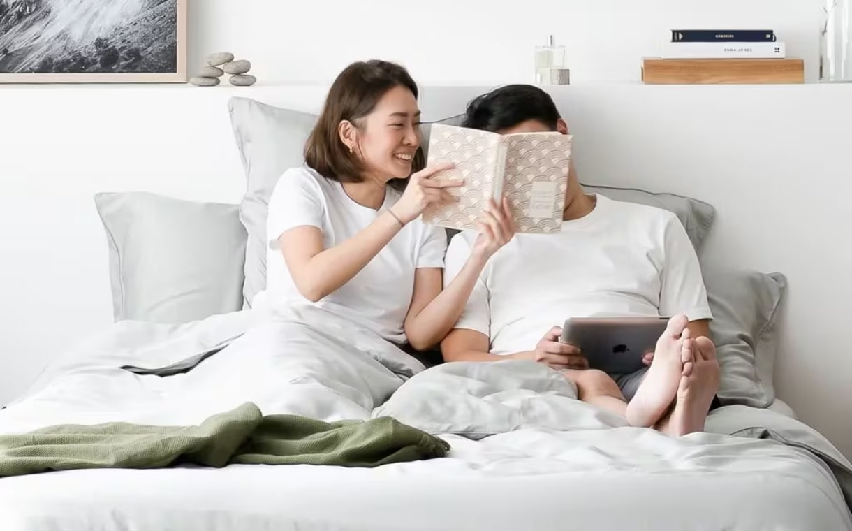 couple reading a book on bed with Weavve's grey tencel sheets