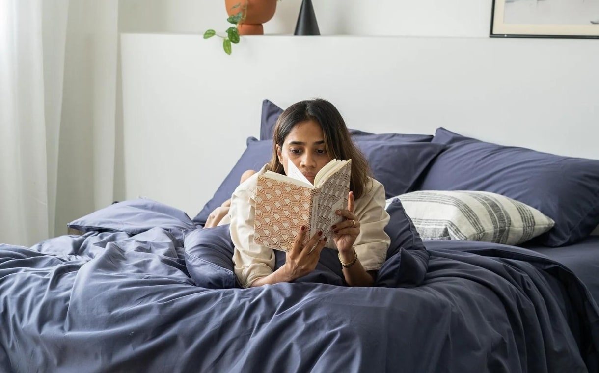 girl reading notebook while lying on blue cotton sheets
