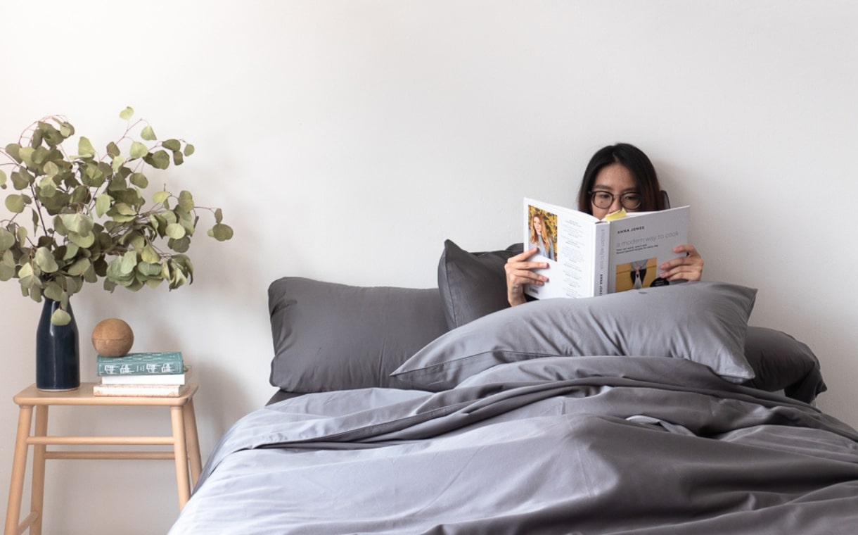 girl reading while sitting on bed with Weavve's cotton bedding