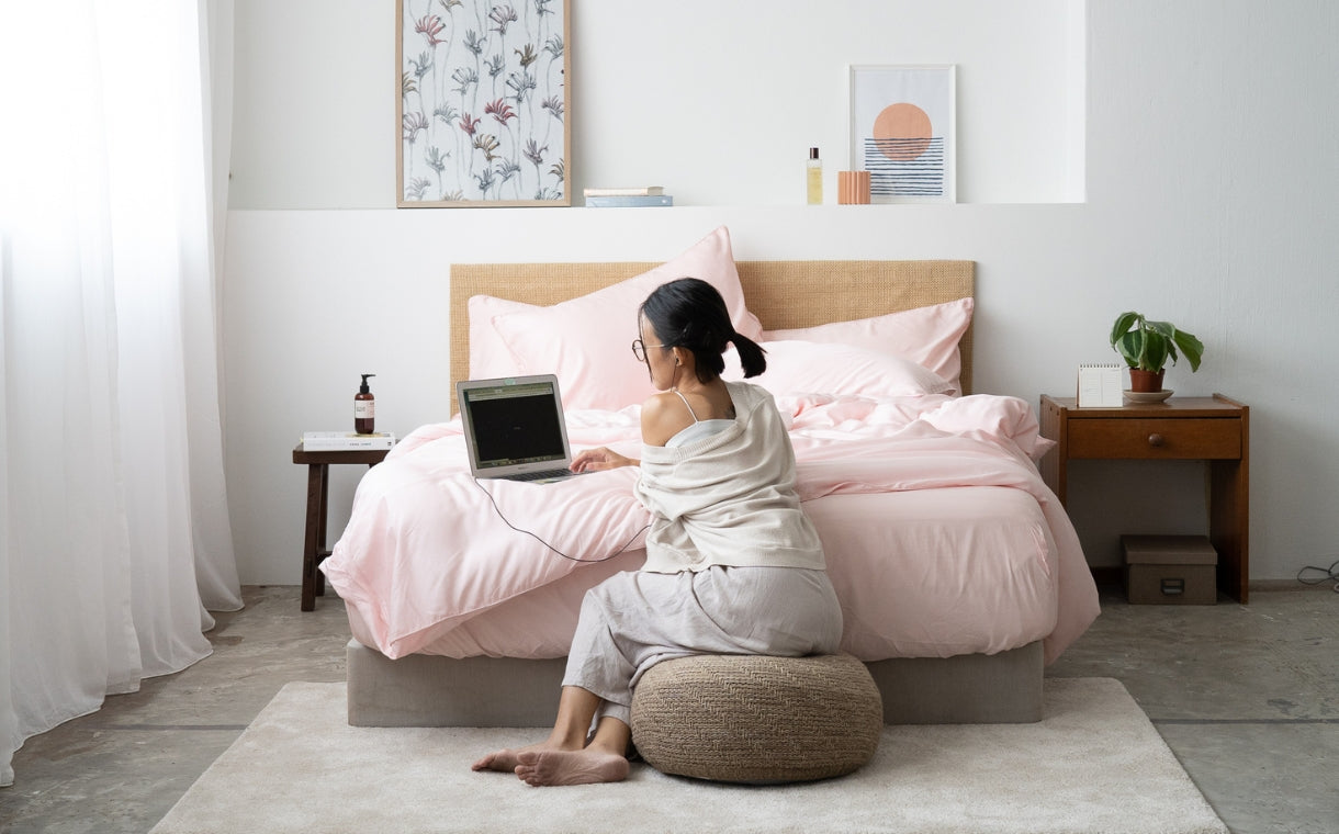 girl sitting on a lounge chair while using laptop on a pink bed