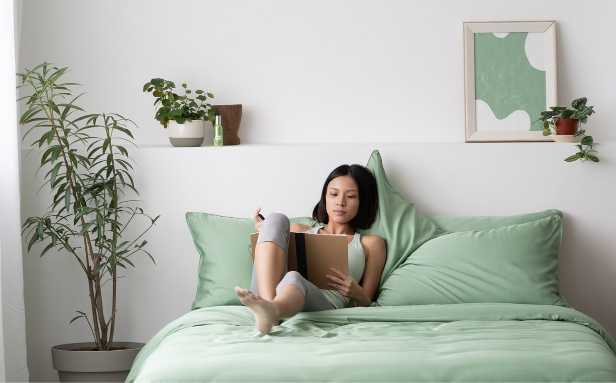 girl writing on her notebook while lying on weavve's tencel sheets