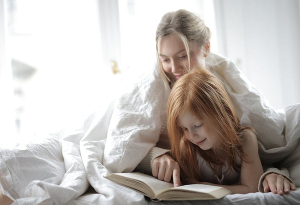 woman and child reading a book while under a duvet