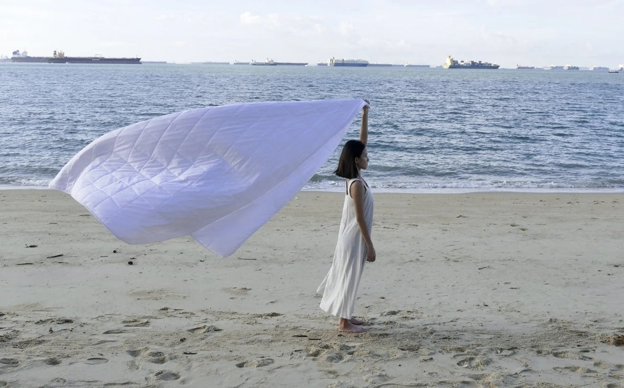 woman holding lightweight duvet being blown by the beach breeze