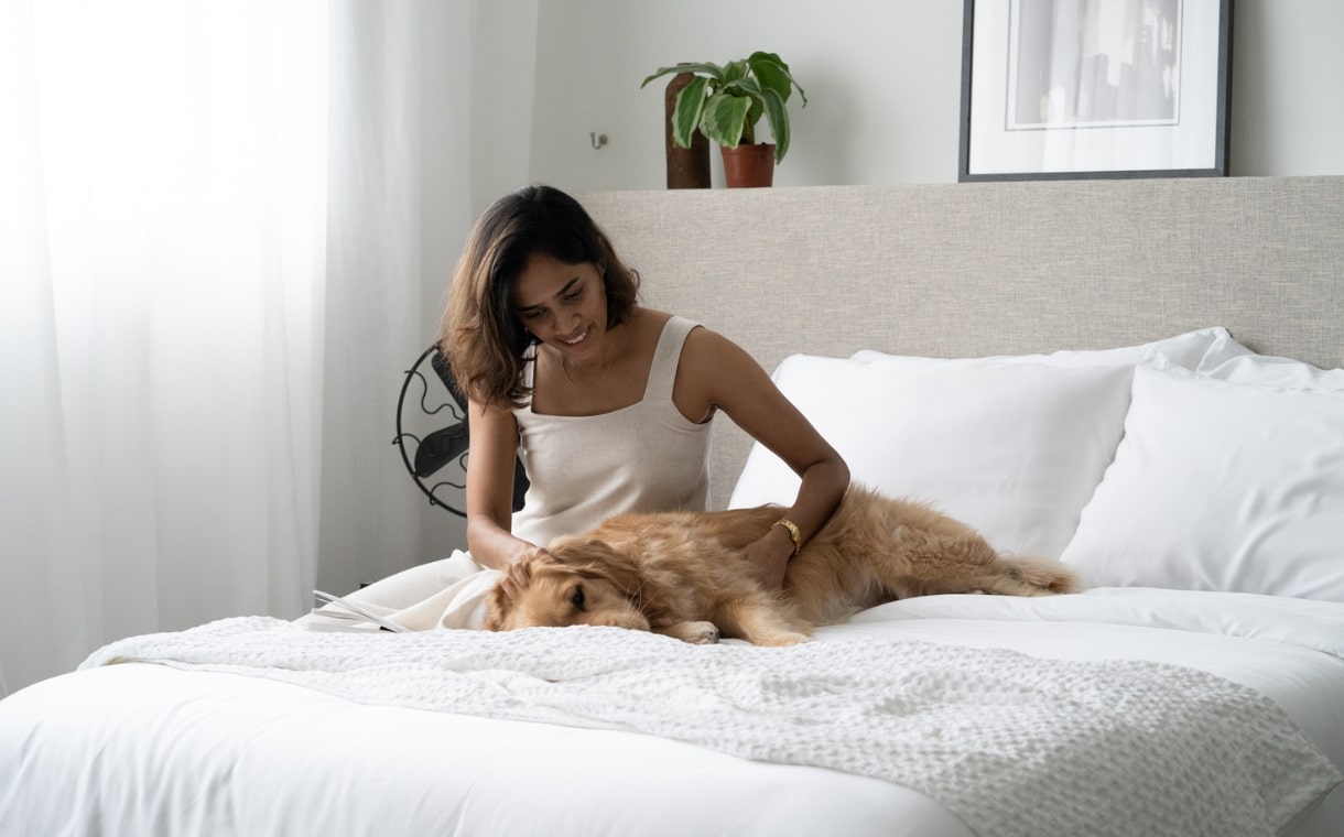 woman petting her dog on bed with weavve's white sheets