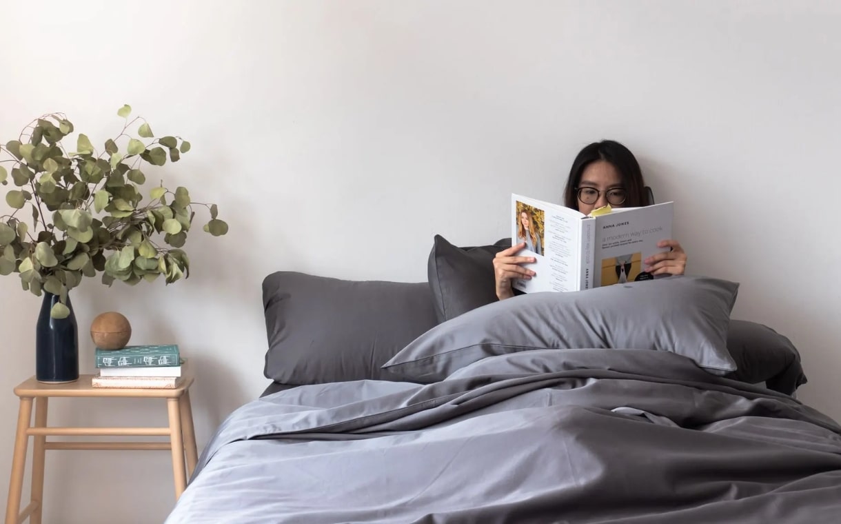 woman reading a book featuring weavve's grey cotton sheets