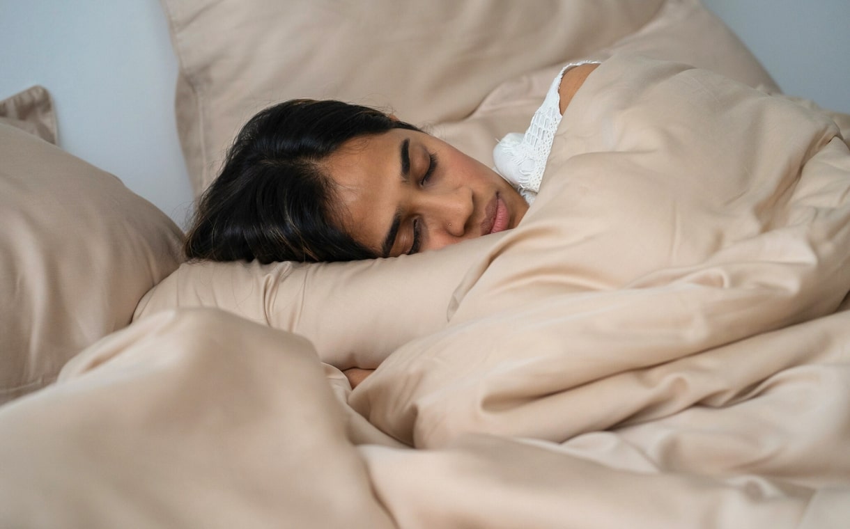 woman sleeping under silky brown blanket and sheets