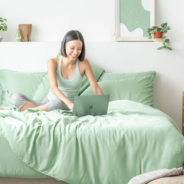 woman using laptop while sitting on fern green TENCEL™ sheets