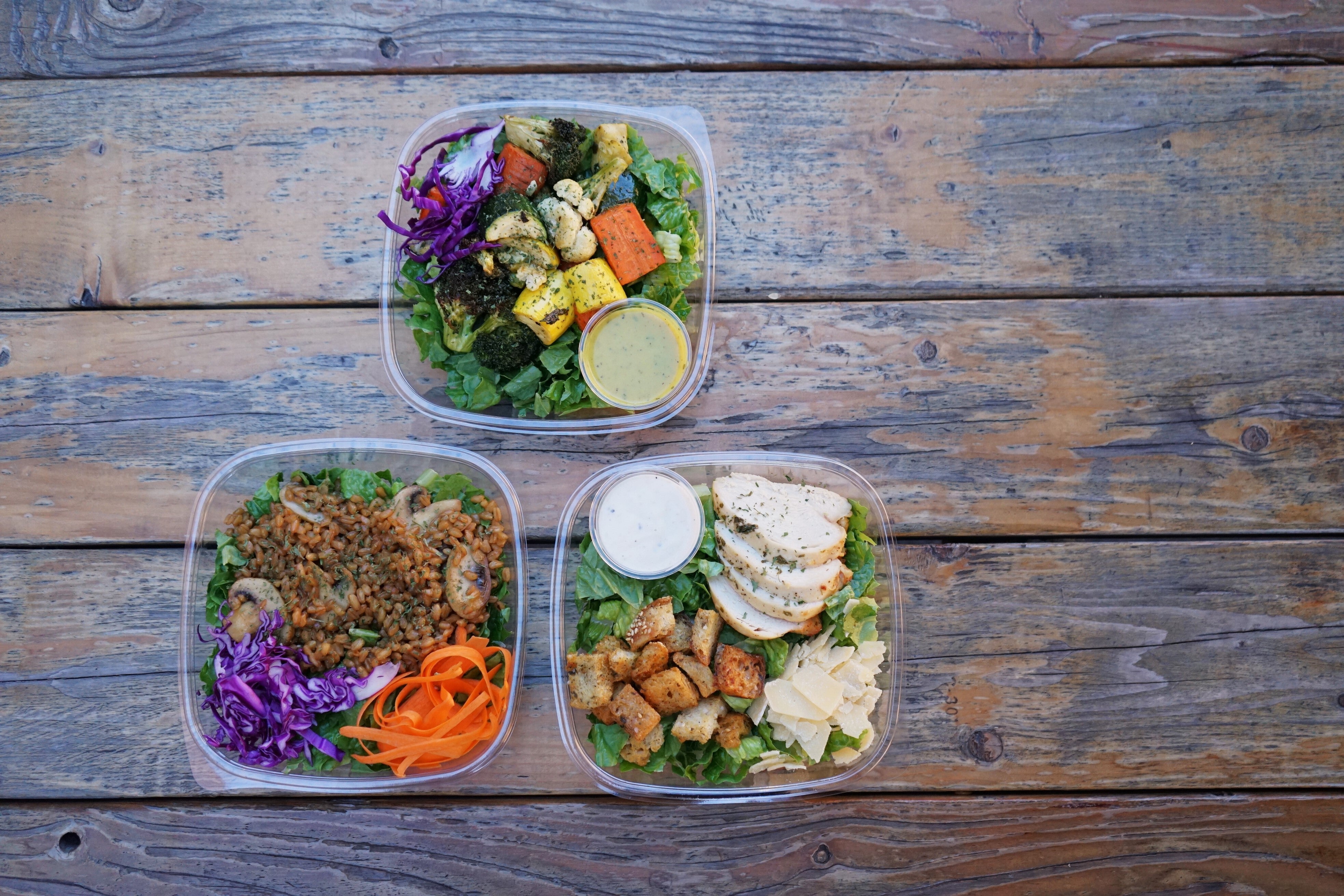 Three salads in to-go containers on a table