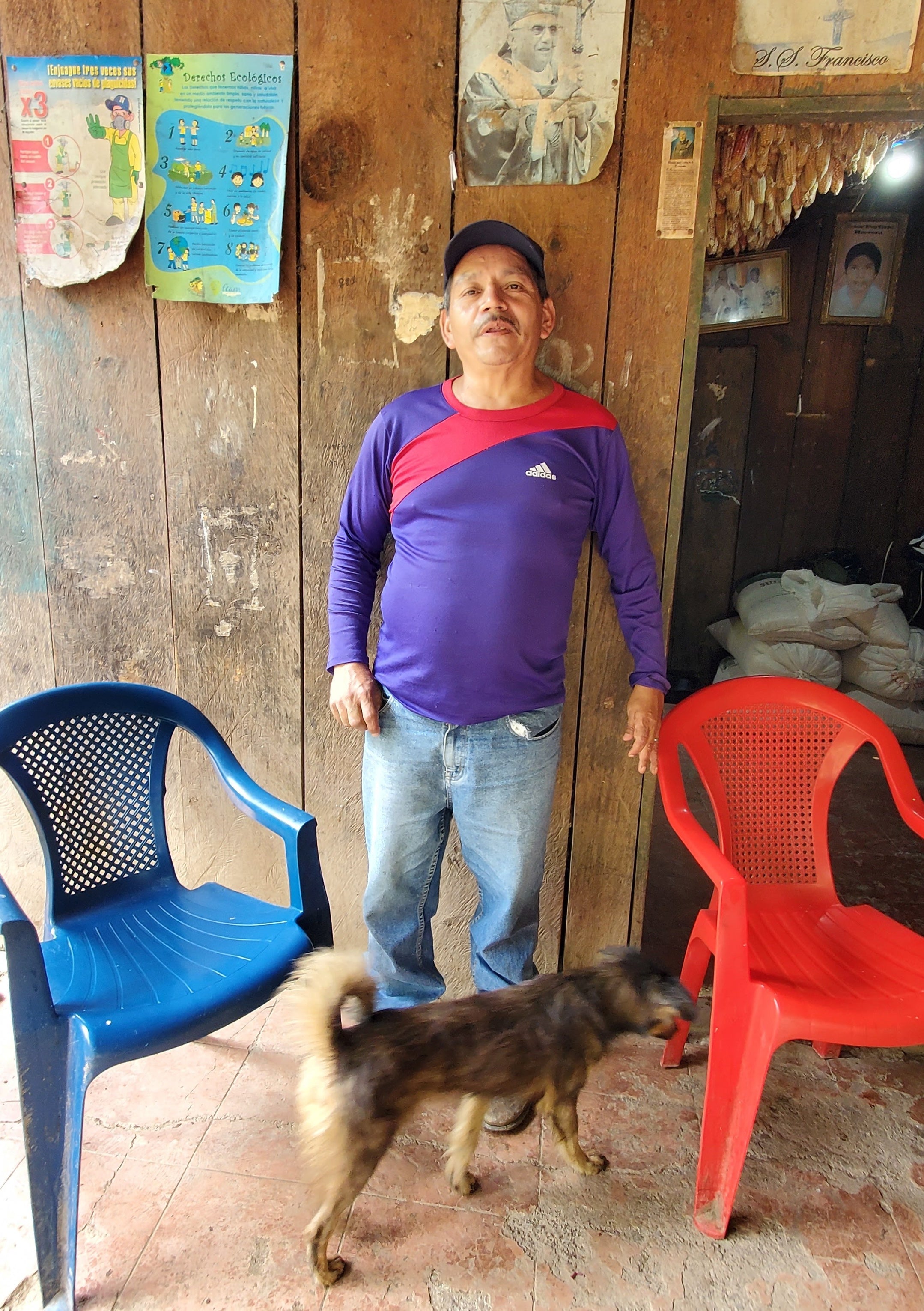 Hector standing against a wall in his home, with a dog trotting by