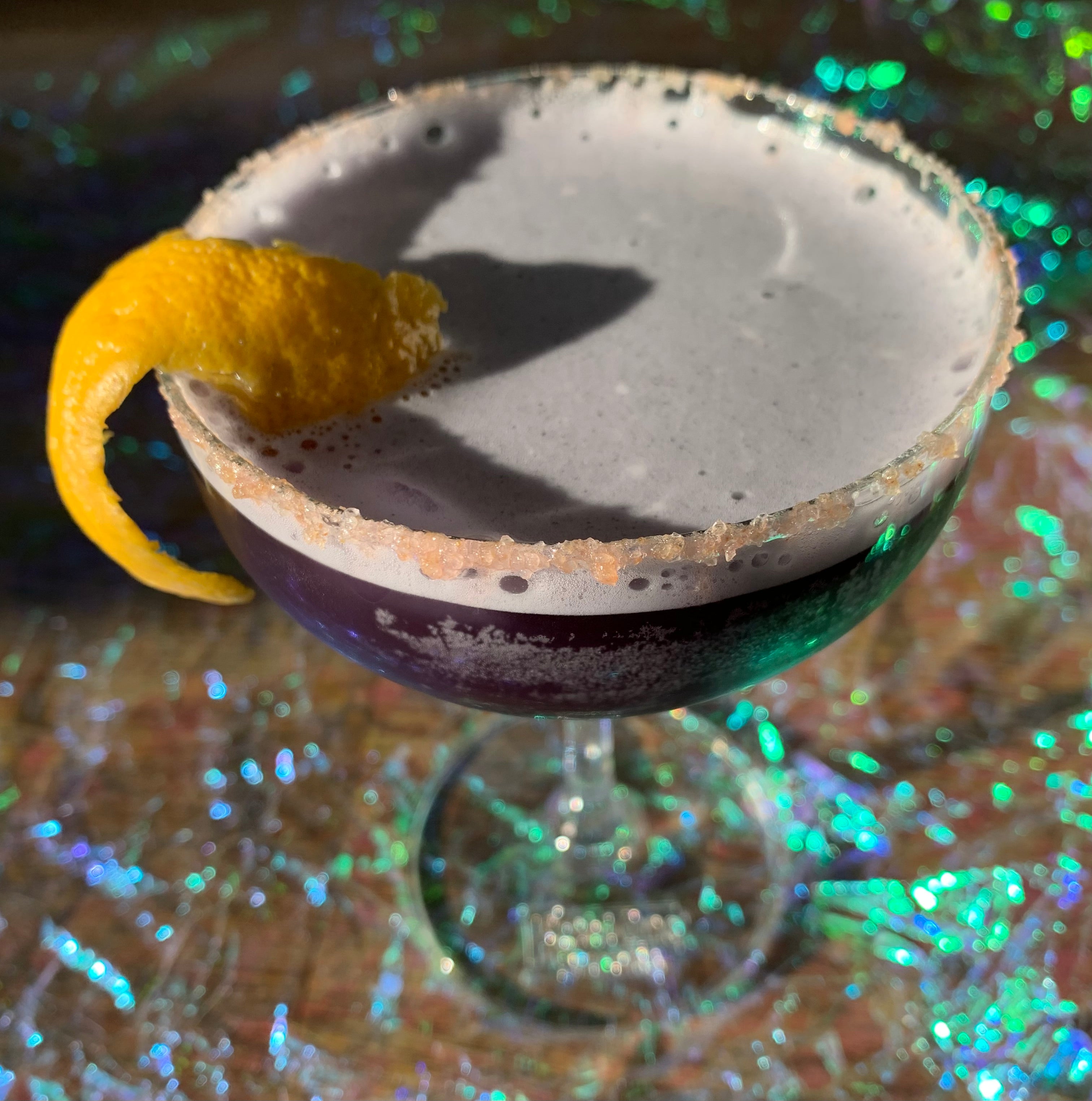 Blue-purple drink in martini glass rimmed with salt and a lemon rind