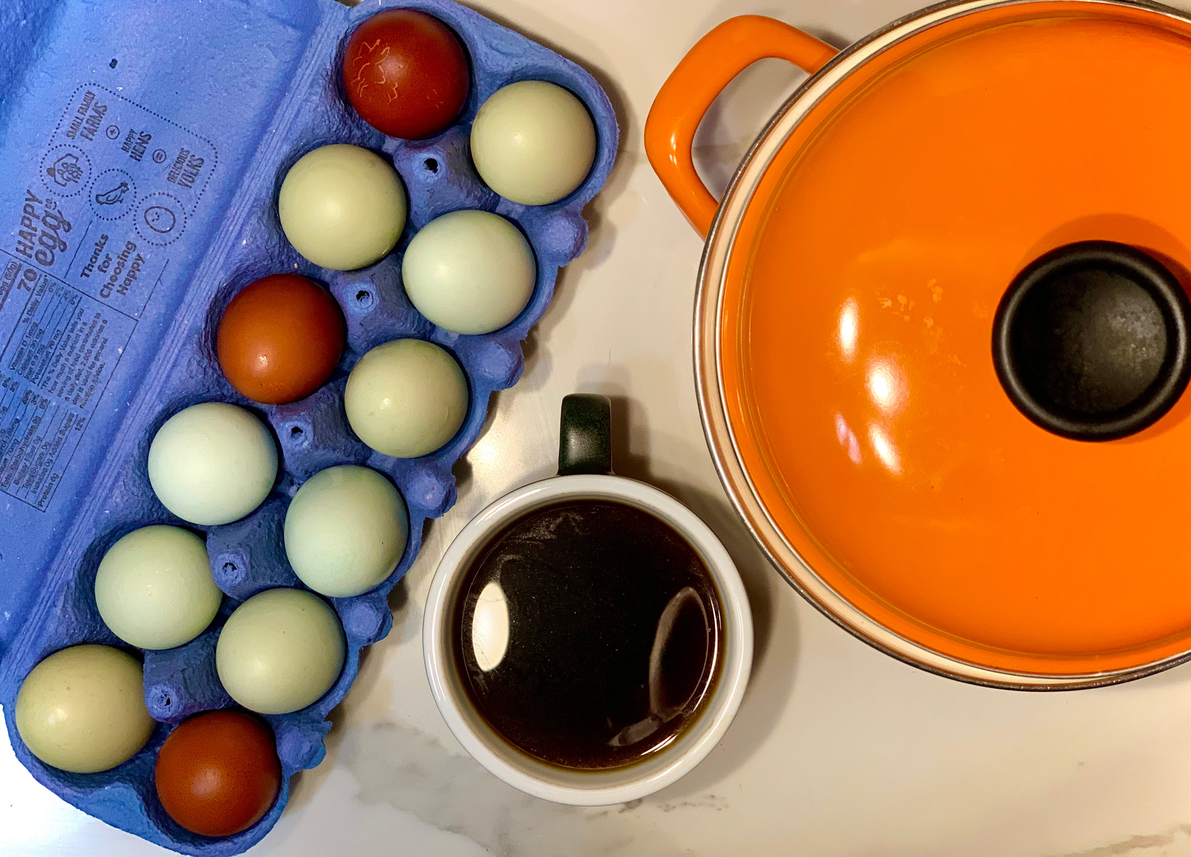 photo of ceramic coffee cup, large orange pot, and carton of colorful eggs 