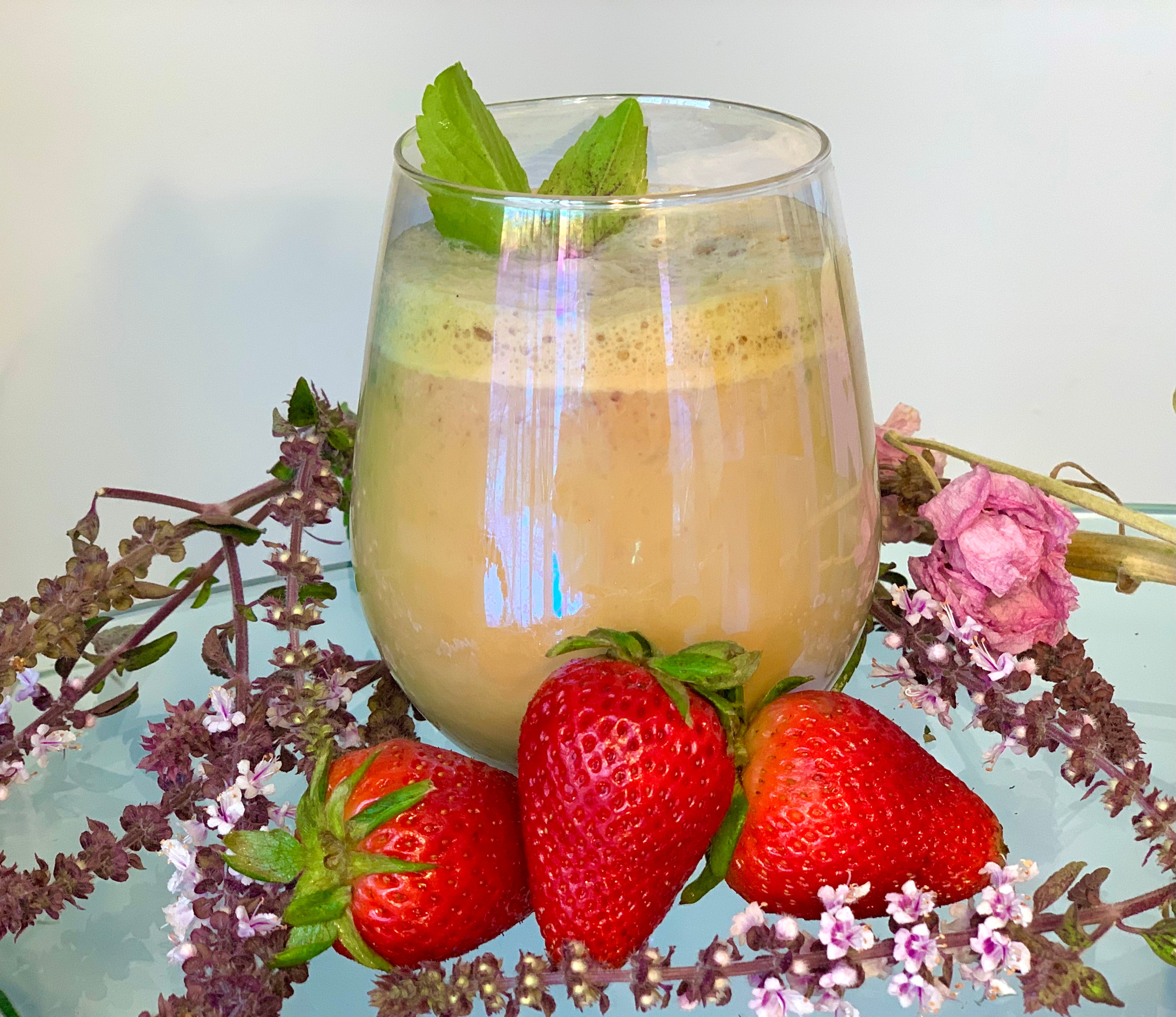 Iced latte in a glass cup surrounded by three strawberries and springs of flowering basil 