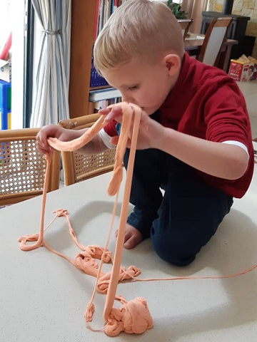 boy on top of a table playing with orange magic stretchy sand 