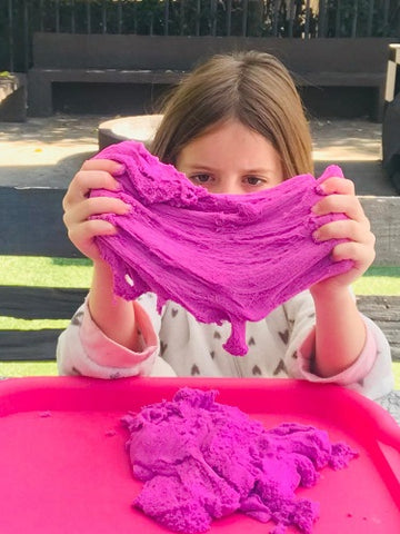 girl sitting outside playing with purple magic stretch sand