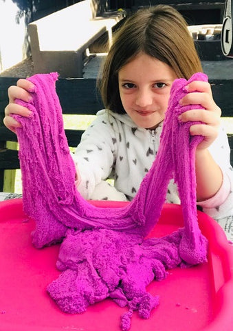 girl sitting outside smiling with purple strechy sand