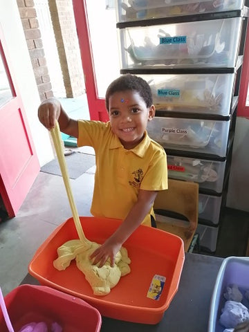 boy wearing a yellow top stretching yellow magic sand